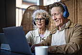 Senior couple sitting in cafe working on digital tablet and laptop