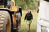 Young female construction worker walking next to excavator