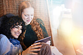 Smiling female friends looking tv show or social media on cell phone