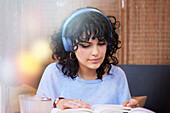 Junge Frau mit Kopfhörern hört Musik oder Podcast und liest ein Buch