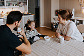 Mother and father sitting with disabled child in wheelchair at kitchen table