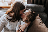Mother hugging and kissing disabled child on sofa