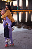 Young woman giving friend or girlfriend piggyback ride, man taking photo