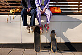 Low section of two women sitting near skateboards