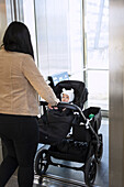 Rear view of woman on parental leave pushing pram with baby inside lift