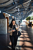 Smiling woman using cell phone while walking at train station