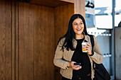 Smiling woman at train station holding disposable cup