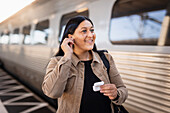 Mid adult woman at train station using earphones