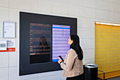 Woman at railway station looking at arrival and departure board on screen