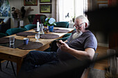 Älterer Mann sitzt am Esstisch und benutzt sein Handy
