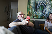 Älterer Mann auf Sofa, der ein Handy benutzt