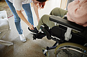 Mutter hilft behinderter Tochter im Rollstuhl beim Anziehen der Schuhe