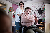 Mother brushing disabled daughter's hair in bedroom