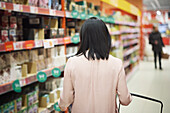 Rear view of woman looking at prices during inflation while doing shopping in supermarket