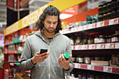 Man in supermarket comparing prices during inflation on cell phone