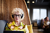 Ältere Frau mit Kopfhörern und Tablet im Cafe