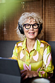 Porträt einer lächelnden älteren Frau mit Kopfhörern, die ein Tablet benutzt