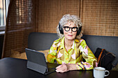 Porträt einer älteren Frau mit Kopfhörern am Tablet