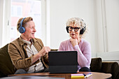 Älterer Mann und Frau sprechen miteinander, während sie im Wohnzimmer sitzen und ein digitales Tablet benutzen, um einen Podcast zu bearbeiten