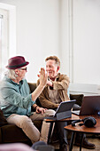 Ältere Männer geben sich gegenseitig ein High-Five, während sie im Wohnzimmer vor einem digitalen Tablet sitzen