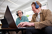 Ältere Männer reden miteinander, während sie im Wohnzimmer sitzen und einen Laptop benutzen, um einen Podcast zu bearbeiten
