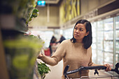 Woman in supermarket looking at fresh herbs while doing shopping