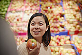 Lächelnde Frau im Supermarkt hält roten und gelben Apfel