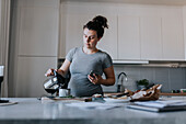 Schwangere Frau gießt Kaffee zum Frühstück ein