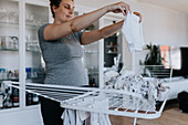 Schwangere Frau bei der Hausarbeit und beim Aufhängen von Babykleidung auf dem Wäscheständer