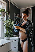 Schwangere Frau faltet Babykleidung und bereitet sich auf die Ankunft des Babys vor