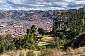 Cusco, elevated view of the rooftops of Cusco city, terraces on the hillsides, and woodland. 