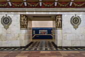 Narvskaya subway station in the city, built in the neoclassical style lined in white marble with many bronze inserts and a decorative frieze, a train moving past a platform. 