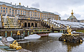 Die Fassade des Peterhofer Sommerpalastes der Romanow-Zaren, Springbrunnen in den Gärten und stilles klares Wasser, leichter Schnee auf Formschnittbüschen.
