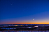 This is the line-up of planets across the southwestern sky on December 6, 2021, consisting of (L to R): Jupiter, Saturn and Venus, with the 2.5-day-old waxing crescent Moon in conjunction below Venus. The Moon had eclipsed the Sun two days before on December 4, when it was on the ecliptic. Two days later it was below the ecliptic line. Jupiter and Saturn are in Capricornus, with its stars all visible here in the evening twilight. The three planets are nicely equally spaced. Such an array makes the ecliptic line visible.