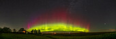 An arc of a Kp4 level aurora on August 28, 2022, from home in southern Alberta (latitude 51° N), showing the classic oxygen greens topped by oxygen reds, but with magentas and blues at left to the northwest where sunlight might still be interacting with the auroral curtains.