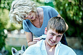 Porträt einer Mutter, die einem jungen kaukasischen Jungen draußen im Garten die Haare schneidet. Lebensstil-Konzept.