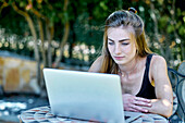 Portrait of a young caucasian woman posing outdoor in a garden with a laptop looking for information in internet. Lifestyle concept.