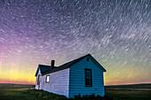 Circumpolar star trails at dawn over the historic Butala homestead at the Old Man on His Back Prairie and Heritage Conservation Area in southwest Saskatchewan, taken May 2015. This is a stack of 70 frames from a larger time-lapse sequence, from the start of the sequence in the dusk twilight, with some aurora active and adding green and magenta to the sky. Cassiopeia is at left over the house.