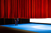 Ein Schauspieler halb verdeckt durch den Vorhang am Ende eines Theaterstücks in einem Schauspielhaus