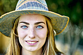 Natürliche Schönheit Porträt einer jungen Frau in den 20er Jahren mit langen Haaren und blauen Augen, die einen Hut im Freien in einem Garten trägt. Lebensstil-Konzept.