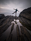 Ein Mann, der auf einem Bein auf den Felsen balanciert und sein Spiegelbild in einem Wasserbecken, Spanien, Europa