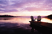 USA, New York State, Saranac Lake, Silhouettes of adirondack chairs on pier at Lake Placid at sunrise in Adirondack Park