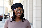 Portrait einer lächelnden Frau mit Brille und Baskenmütze in der Stadt