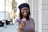 Porträt einer lächelnden Frau, die den Abstimmungsknopf in der Stadt zeigt
