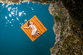 Blick von oben auf eine Frau, die auf einem Schwimmdock in der Nähe der felsigen Küste liegt