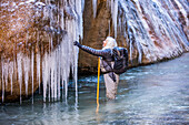 USA, Utah, Springdale, Zion National Park, Ältere Frau erkundet Eiszapfen beim Wandern in den Bergen