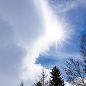 USA, Idaho, Hailey, Sonne scheint durch Wolken mit Bäumen im Vordergrund