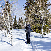 USA, Idaho, Sun Valley, Ältere Frau mit Schneeschuhen beim Wandern im verschneiten Wald