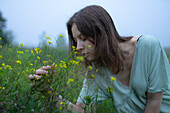 Frau riecht an Blumen auf einer Wiese an einem nebligen Tag