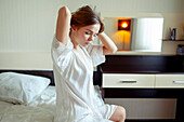 Junge Frau im Pyjama auf dem Bett sitzend